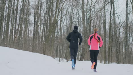 A-beautiful-woman-and-a-man-are-running-in-the-forest-in-winter-proper-nutrition-and-a-healthy-lifestyle.-Slow-motion.
